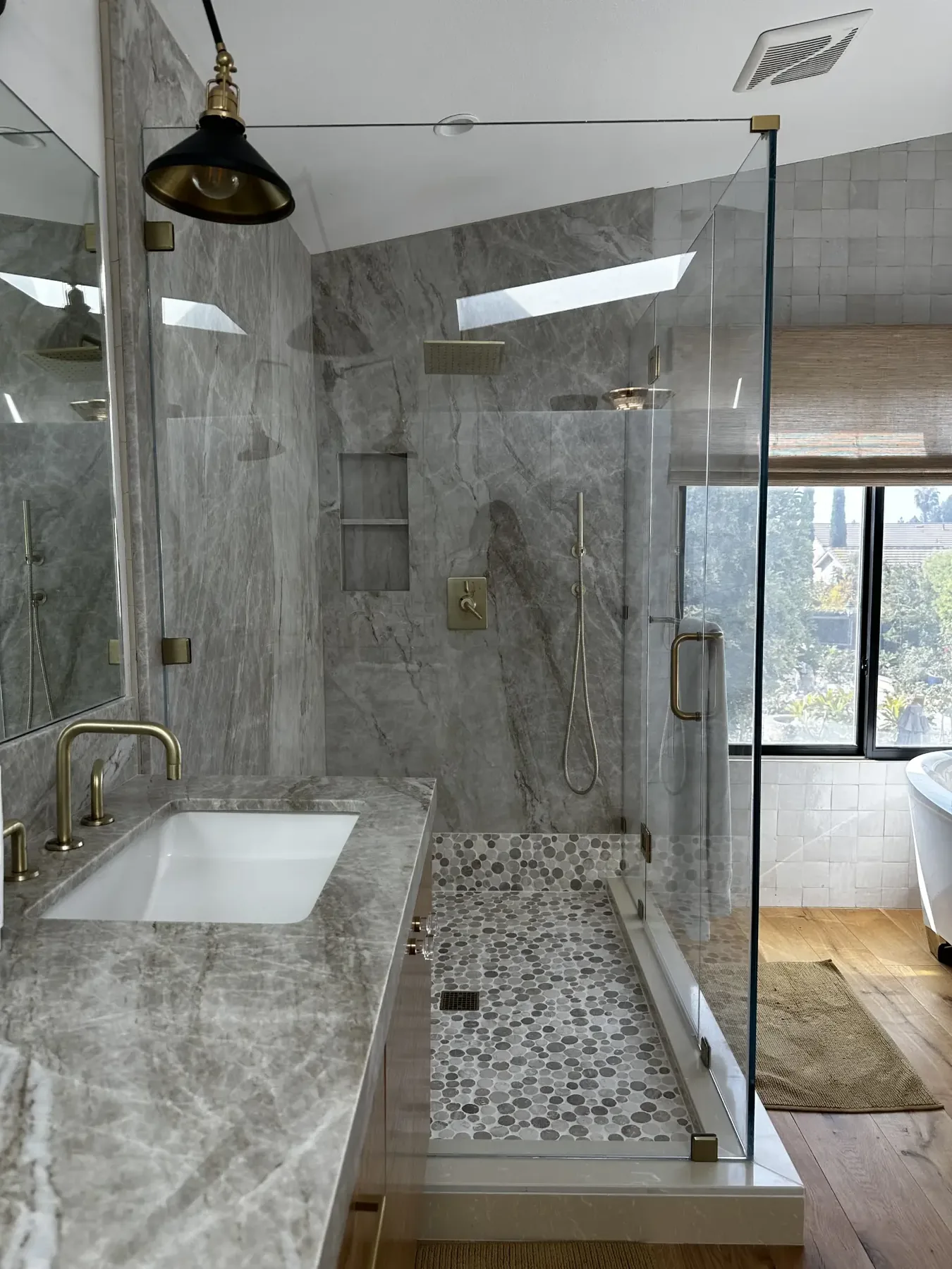 Marble master bathroom with brass fixtures, frameless glass shower and pebble tile floor, remodeled by Laguna Bay Developing