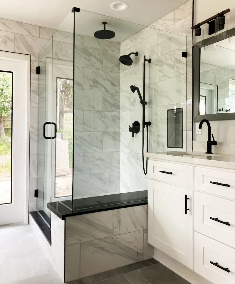 Modern bathroom remodel with marble tile shower, black fixtures and white vanity cabinets