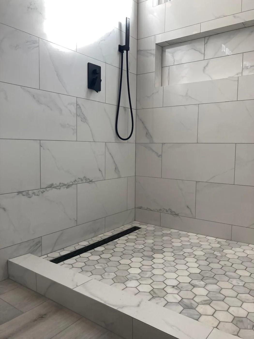 Walk-in shower with marble-look tile walls, hexagonal mosaic floor and black linear drain