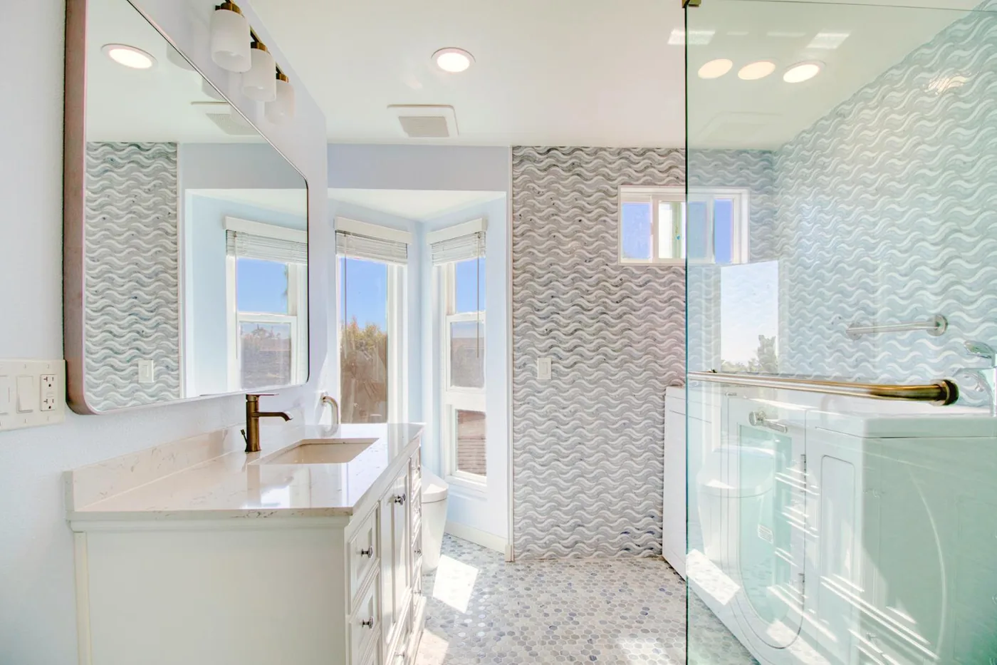 Bright coastal bathroom with wave-pattern tile walls, white vanity and glass shower enclosure