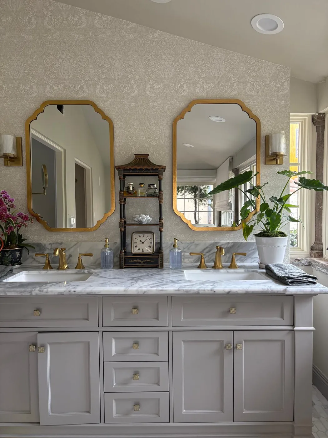 Bathroom vanity with grey cabinets, marble countertop, gold octagonal mirrors and brass faucets